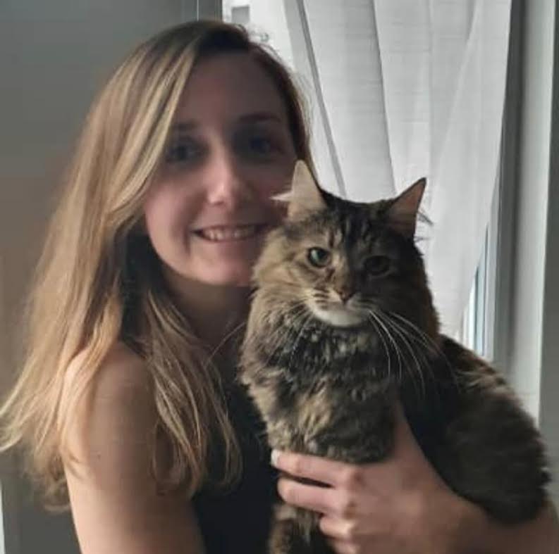 Femme souriante aux longs cheveux blonds tenant un chat tigré à poil long dans ses bras.